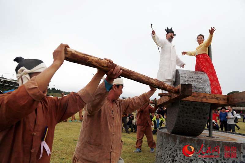 民俗節(jié)上，兩名身著華麗服裝的人站在“石磨”上載歌載舞