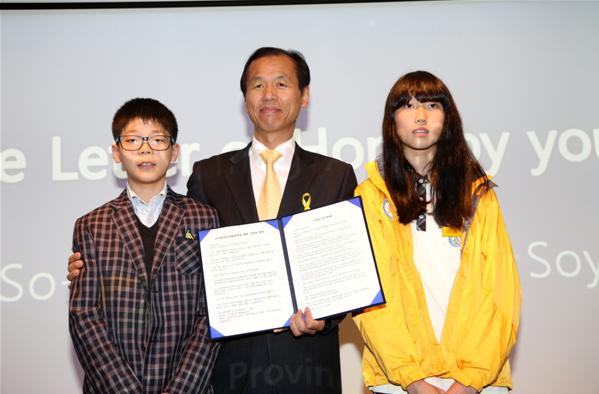 學(xué)生們在2014年4月28日召開的2018年平昌冬奧會賽場建設(shè)促進情況新聞發(fā)布會上朗讀信件，祝愿冬奧會成功舉辦。江原道知事崔文洵與學(xué)生們合影留念。